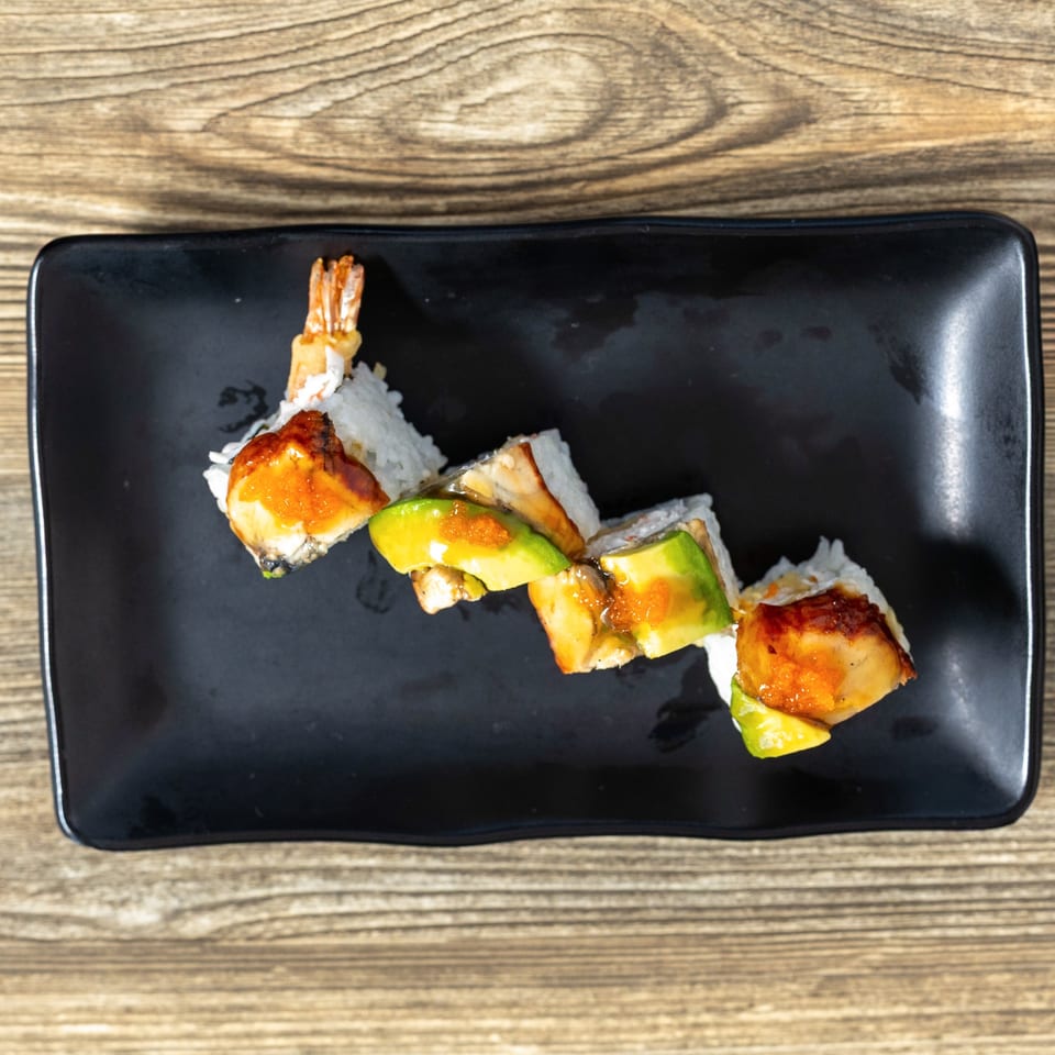 Sushi Hana's dragon roll with shrimp tempura, avocado, eel, and roe on a black plate.