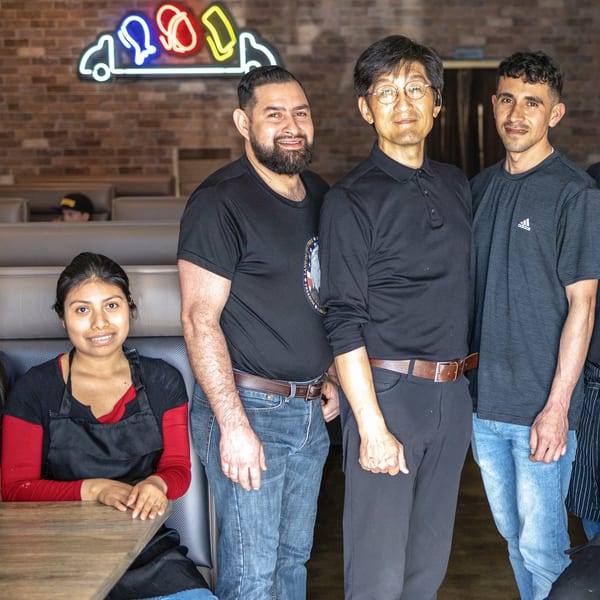 Four Sushi Hana staff members, three men and one woman, smiling in the restaurant dining area.