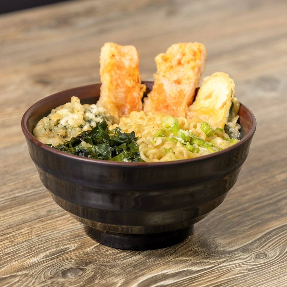 A bowl of ramen with noodles, green onions, seaweed, and three pieces of tempura.