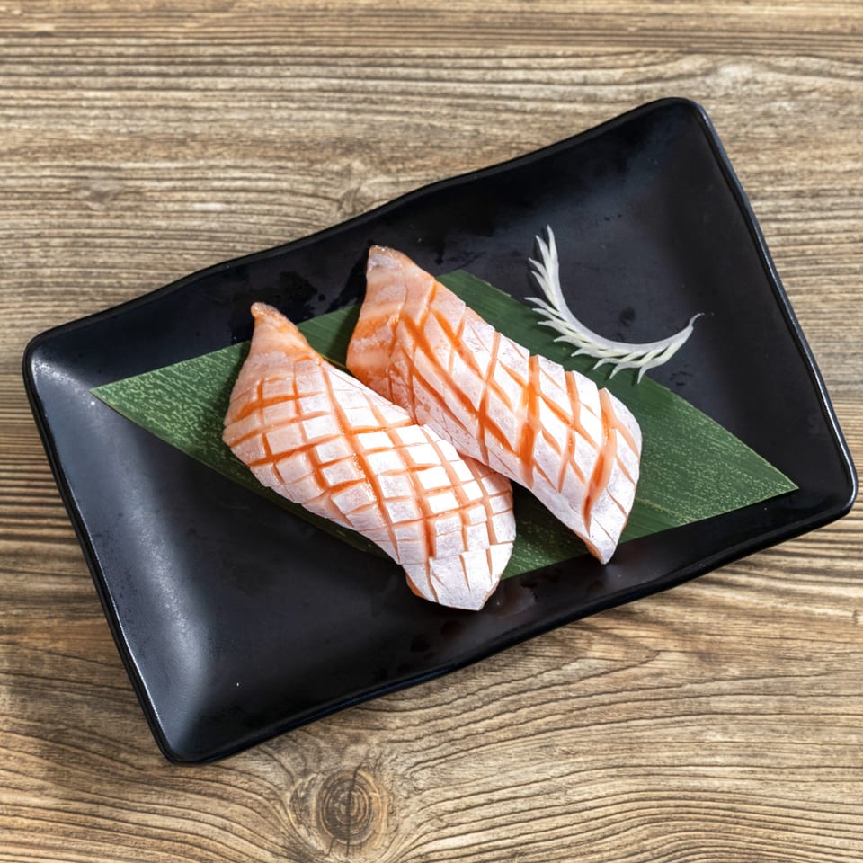 Two pieces of seared salmon nigiri with crosshatch scoring, served on a black plate with a green leaf.