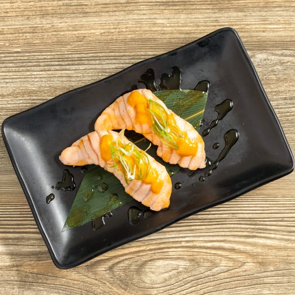 Two pieces of Sushi Hana salmon nigiri with orange sauce and green onions on a black plate.
