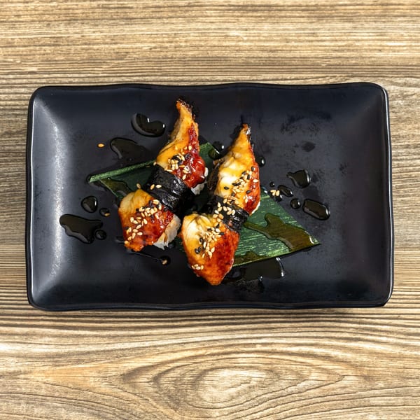 Four pieces of unagi nigiri sushi with sesame seeds on a black rectangular plate.
