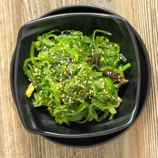 Sushi Hana's vibrant green seaweed salad, topped with white and black sesame seeds, in a black bowl.